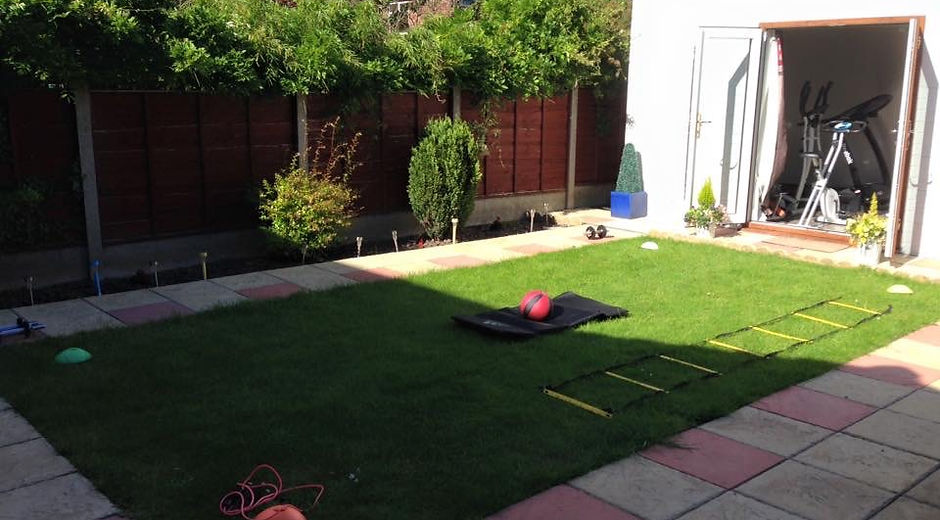 A back garden gym studio. There is a green lawn in sun with an outdoor studio at the far end